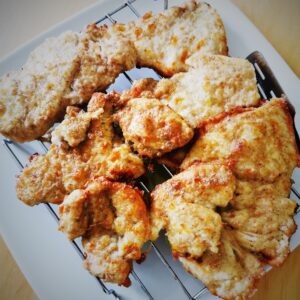pieces of golden coated flattened chicken breast on a wire rack over a white plate