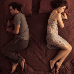 an aerial view of a bed with a man sleeping facing to the left and an awake woman facing to the right