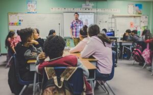 Kids in a classroom being taught with a teacher at a whiteboard