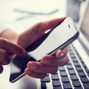 a hand holding a mobile phone about to dial. With a computer keyboard in the background
