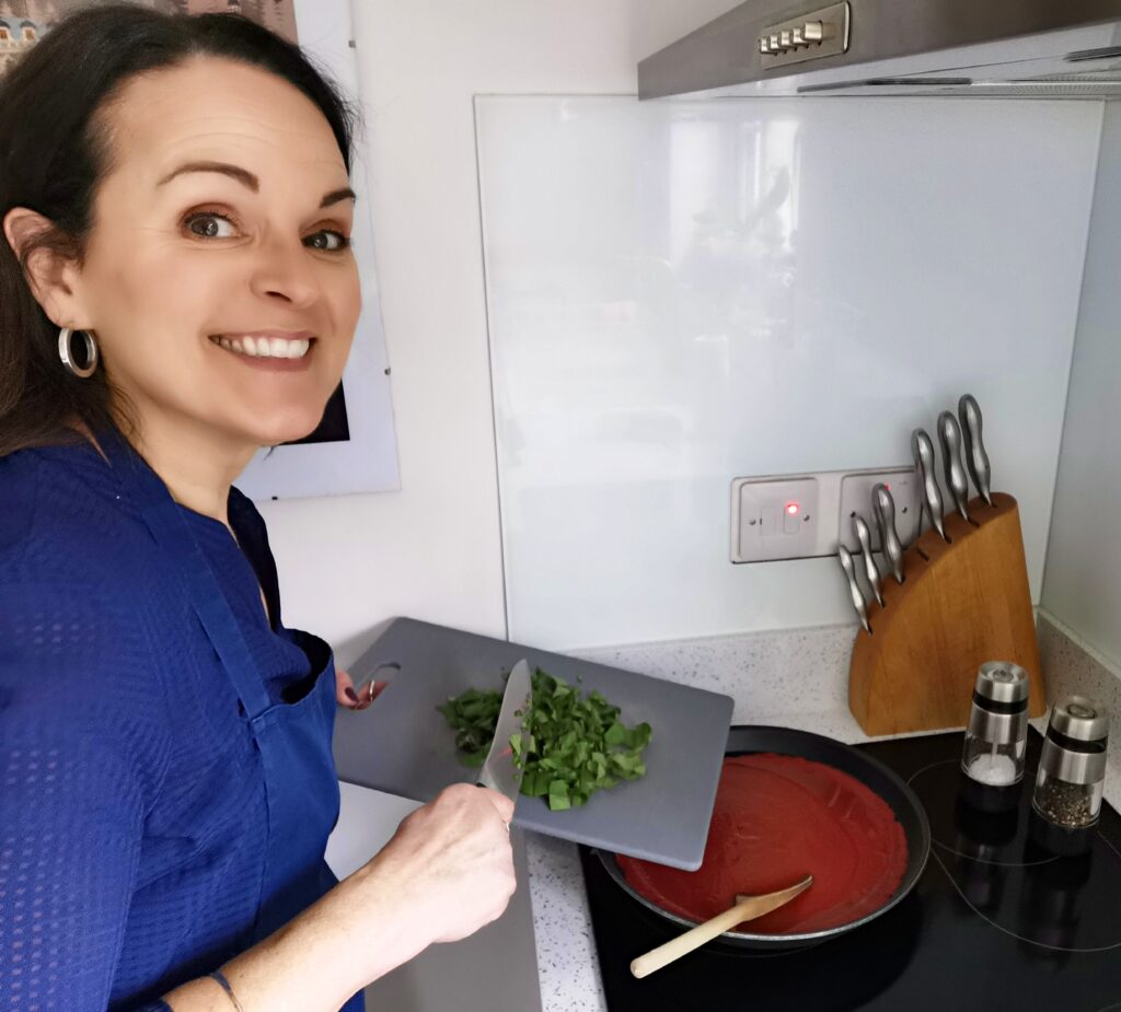 Natasha at the hob scraping basil into a pan of tomato sauce